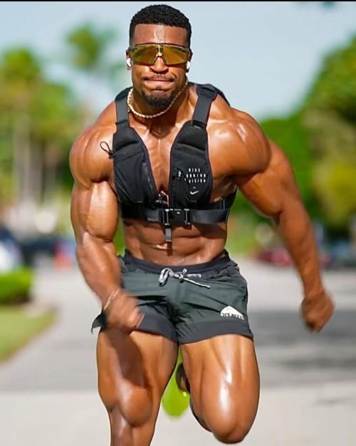 Muscular athlete sprinting in a weighted vest during outdoor workout.