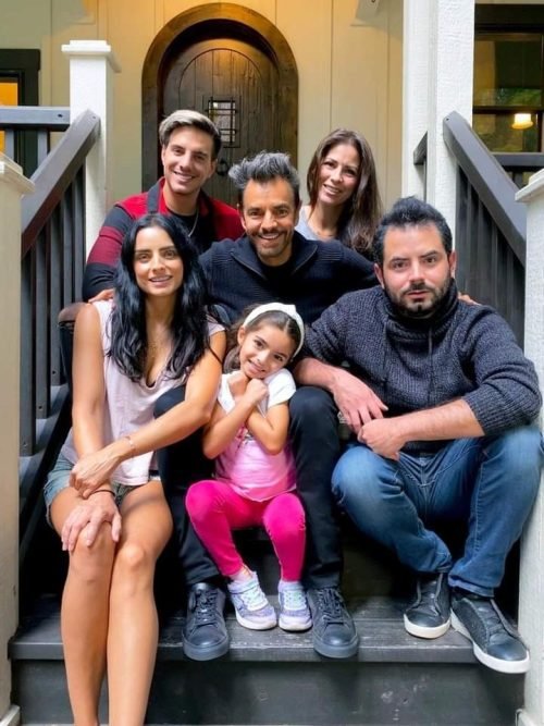 Eugenio Derbez sitting on porch steps with his smiling family.