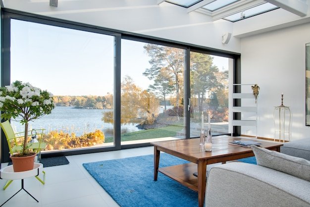 Modern solarium interior with large glass doors overlooking a lake and autumn trees.