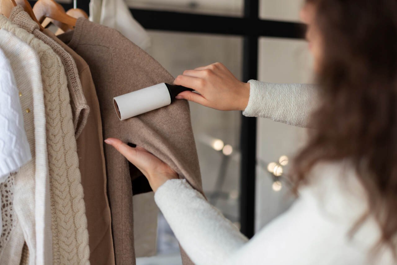 Person using a lint roller on a brown sweater hanging on a rack