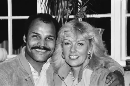 John Conteh with a mustache and his wife posing together indoors.