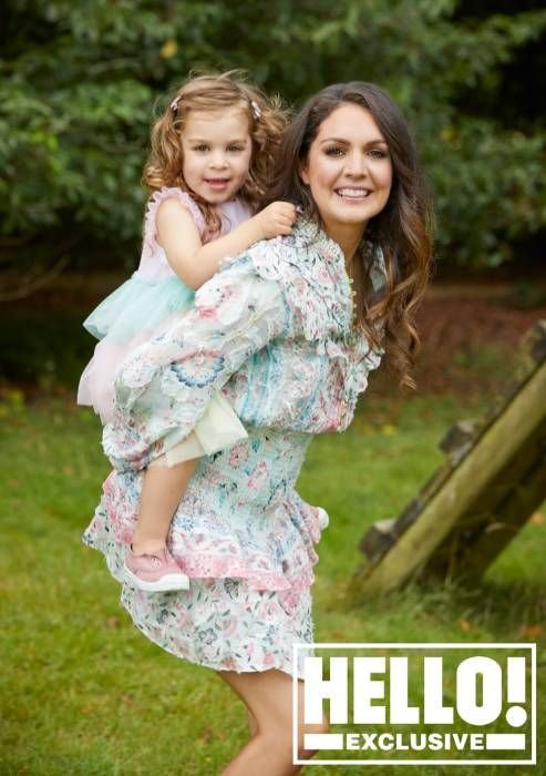 Laura Tobin carrying her young daughter on her back, both smiling in a garden setting.