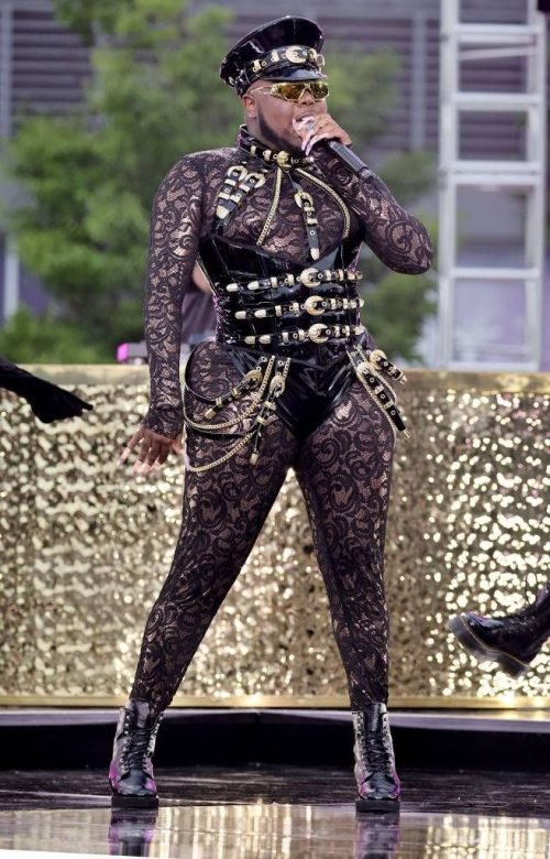 Saucy Santana performing in black lace and leather harness outfit with gold accents.