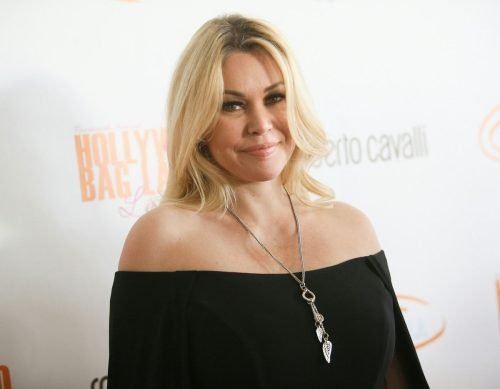 Shanna Moakler smiling on the red carpet in an off-shoulder black dress.