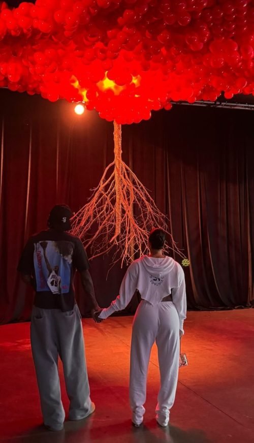 Jalen Green and Draya Michele holding hands in front of red balloon and root art installation.