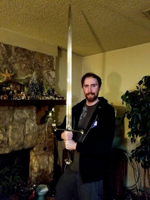 Asmongold holding an oversized sword in a living room decorated with holiday miniatures.