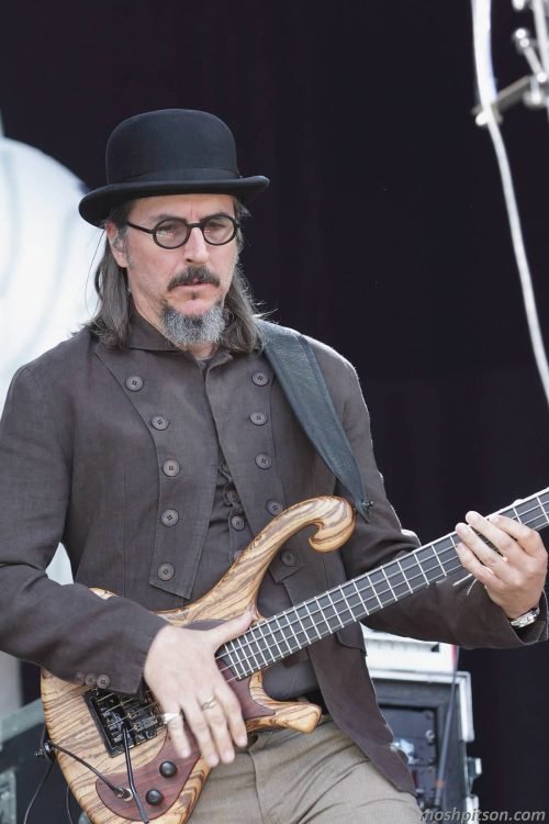 Les Claypool playing a custom wooden bass guitar during a live performance.