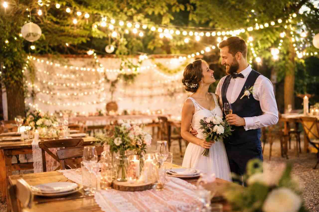Happy couple celebrating a budget-friendly dream wedding in an elegant outdoor venue with floral décor and string lights.
